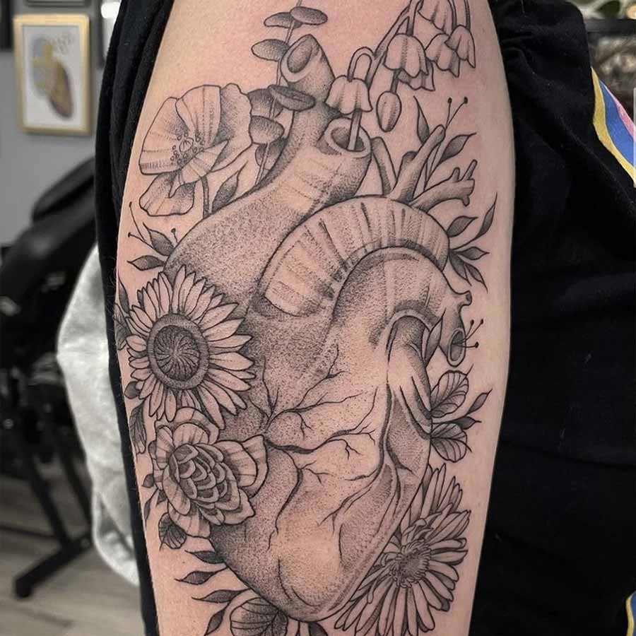 Tatuaggio cuore anatomico che sembra un porta fiori, si intravedono margherite, papaveri e altri tipologie Tatuaggio cuore anatomico che sembra un porta fiori, si intravedono margherite, papaveri e altri tipologie